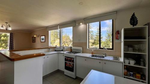a kitchen with white cabinets and a sink and windows at Channers on Norfolk in Burnt Pine