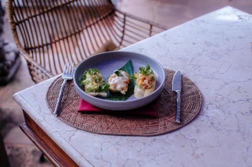 a bowl of food with broccoli on a table at Villa Semana Resort Ubud in Ubud