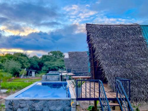 an outdoor swimming pool with a straw roof at Habarana Tree House Ambasewana Resort in Habarana