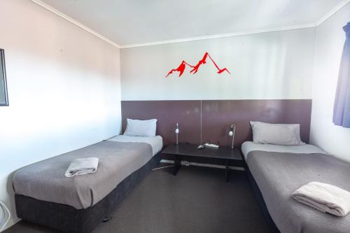 two beds in a room with a red chart on the wall at Ivorytowers Accommodation in Fox Glacier