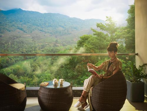 a woman sitting on a chair reading a book in front of a window at The Grand Cliff Resort Munnar in Viripara