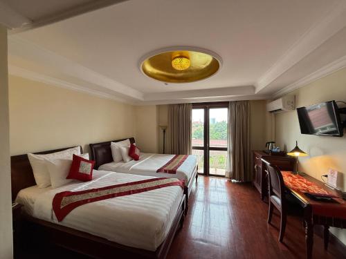 a hotel room with two beds and a desk and a television at Phasouk Vien Chantra Hotel in Vientiane
