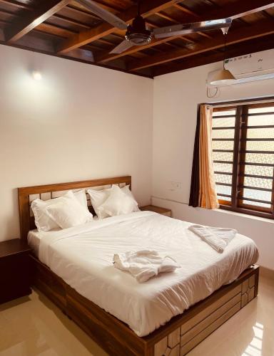 a bedroom with a bed with white sheets and a window at Tropical Island Homestay in Payyannūr