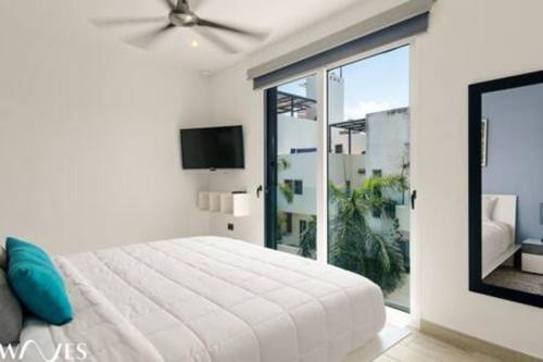 a white bedroom with a bed and a large window at 1 Br. w5th avenue view Steps from the beach in Playa del Carmen