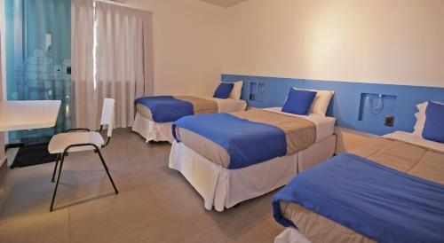 a hotel room with three beds and a chair at Concept Design Hostel & Suites in Foz do Iguaçu