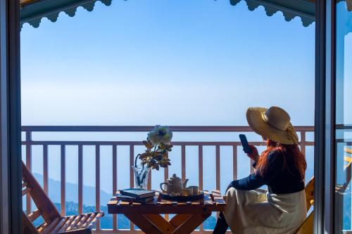 a woman sitting at a table looking out a window at ELIVAAS 3BHK Plus Attic Cliffside Villa with Scenic Views in Kasauli
