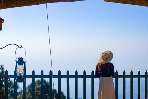 a woman in a hat standing next to a fence at ELIVAAS 3BHK Plus Attic Cliffside Villa with Scenic Views in Kasauli