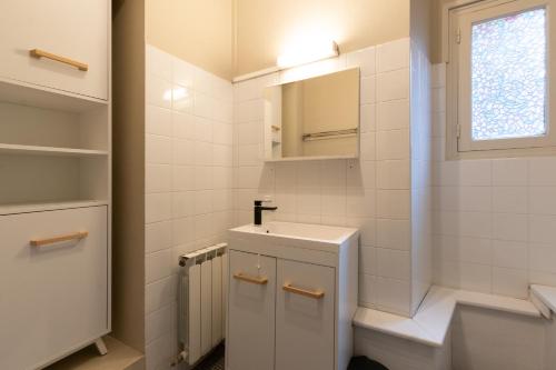 une salle de bain blanche avec un lavabo et un miroir dans l'établissement Logements À 2 PETITS PAS, à Bagnères-de-Bigorre