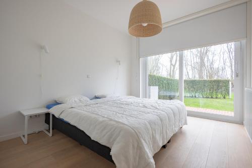 a white bedroom with a bed and a large window at Duinhof VI 6 in Cadzand