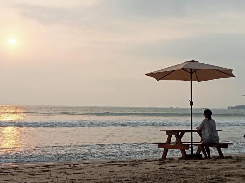 a person sitting on a bench under an umbrella on the beach at Kondominium Pantai Carita selatan pandeglang in Sukarame