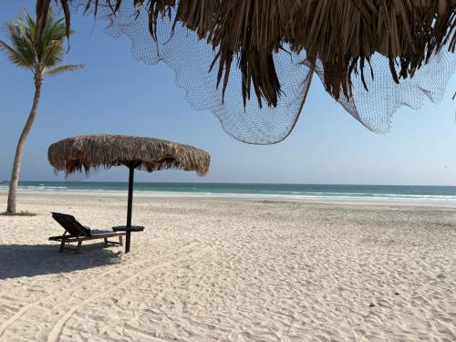 a beach with a chair and an umbrella and a palm tree at Villa Davelin, Hawana Salalah in Salalah