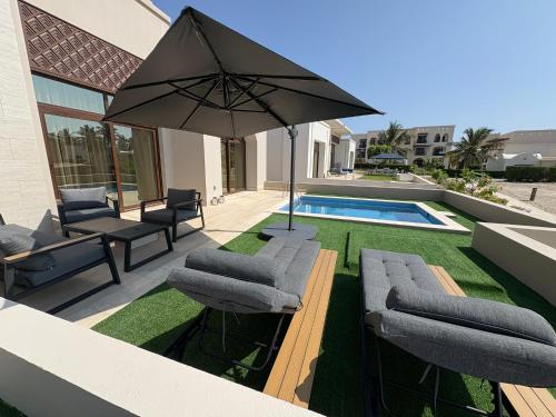 a patio with chairs and an umbrella and a pool at Villa Davelin, Hawana Salalah in Salalah