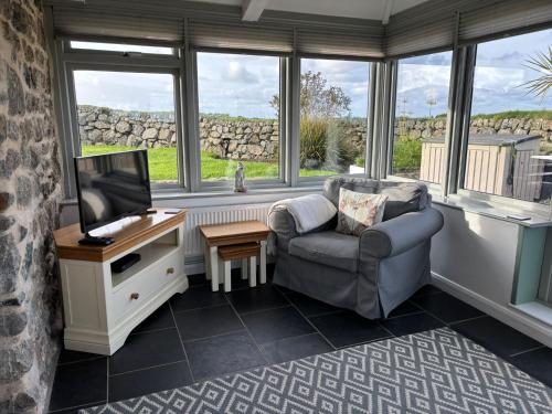 a living room with a chair and a tv and windows at Lower Trowan Cottage in Sharnbrook