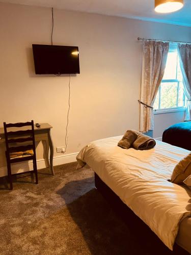 a bedroom with a bed and a desk with a television on the wall at Spacious 5 Bedroom Home in Central Kidderminster with Private Parking and Electric Vehicle Facilities, Easy Access to Birmingham and Nearby Towns in Kidderminster