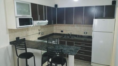 Una cocina con una encimera con sillas y un refrigerador. en Departamento Neuquen, en Neuquén