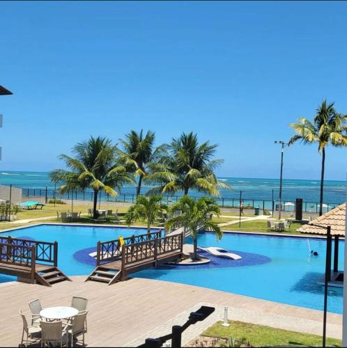 a swimming pool with palm trees and the ocean at MAUÍ BEACH Tamandaré Flat Terreo in Tamandaré