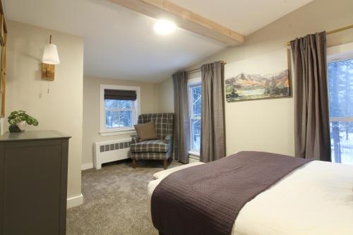 a bedroom with a bed and a chair and windows at The Aurora Inn & Cottages in Bartlett