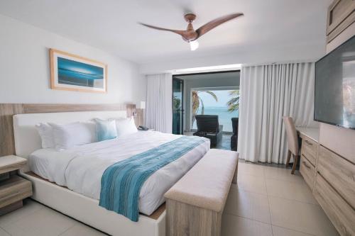 a bedroom with a bed and a television and a balcony at Hodges Bay Resort & Spa, an HQ Luxury Resort & Residences in Saint Johnʼs