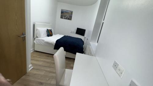 a small white bedroom with a bed and a desk at Sangha Hall in Leicester