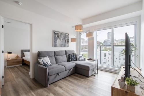 a living room with a gray couch and large windows at Le Panorama - Parking gratuit - Toit terrasse in Quebec City