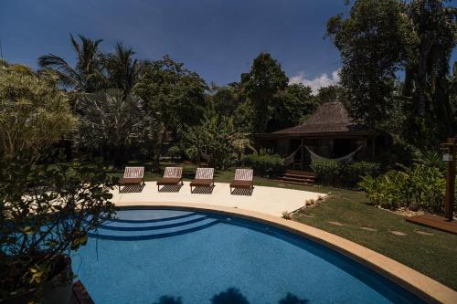 a swimming pool with four chairs and a house at Villa Cozy in Arraial d'Ajuda