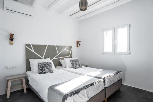 a white bedroom with a large bed with black and white pillows at Mykonos Residence Villas & Suites Merchia beach in Merchia Beach