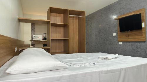 Un dormitorio con una cama blanca con un televisor en la pared. en Victory Flat Tambaú BR, en João Pessoa