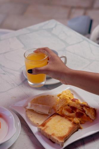 een persoon die een glas sinaasappelsap vasthoudt naast een bord met ontbijtvoedsel bij Hotel Kaamú Taganga in Taganga