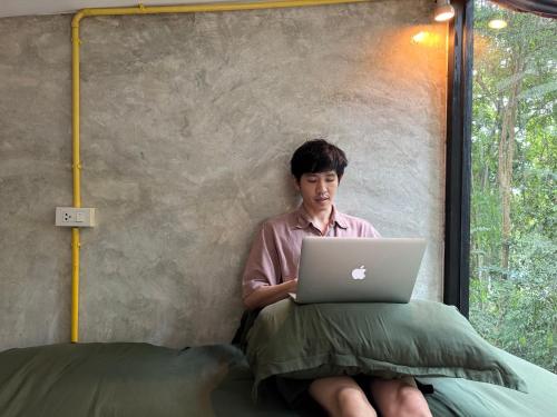 a man sitting in a bed with a laptop at BeachBox@Koh Сhang in Ko Chang