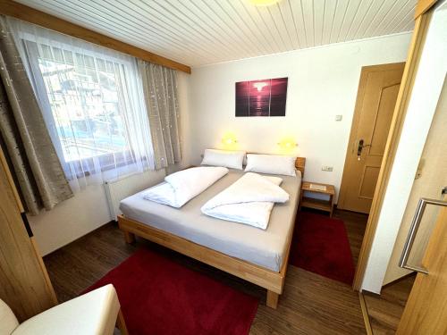 a bedroom with a bed with white pillows and a window at Haus Troger in Sankt Jakob in Defereggen