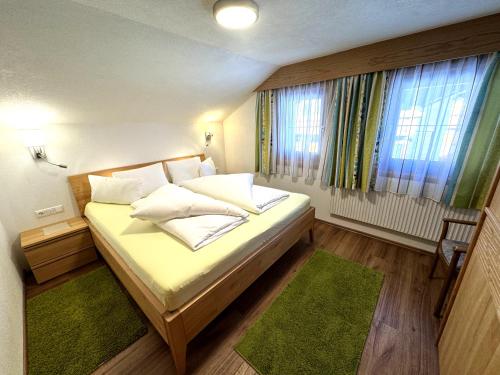 a small bedroom with a bed and two windows at Haus Troger in Sankt Jakob in Defereggen