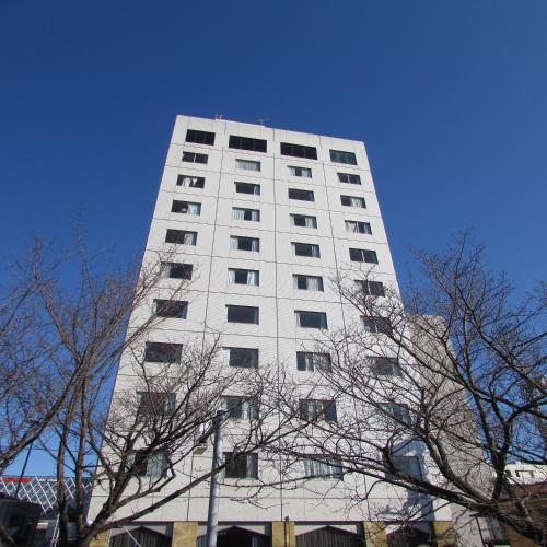 a tall white building with trees in front of it at APA Hotel Mito-Ekimae in Mito