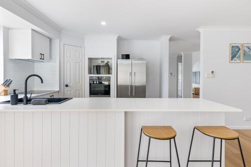 a white kitchen with white cabinets and two bar stools at Stylish 5-Bedroom Home Geographe in Geographe