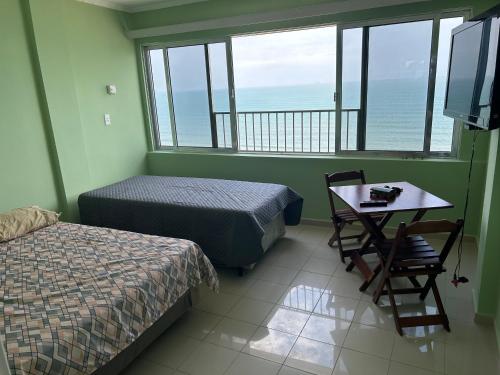 a room with two beds and a table and a television at Apto em frente ao mar prédio redondo linda vista in Peruíbe