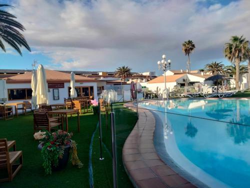 a resort pool with tables and chairs and palm trees at Puerta del sol in Caleta De Fuste