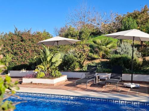 een zwembad met twee parasols en twee stoelen en een tafel bij La Sureña in Alhaurín el Grande