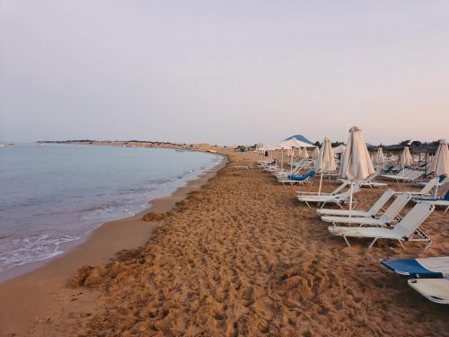 a row of lounge chairs and umbrellas on a beach at Relaxrooms, room with 2 single beds in Agios Georgios
