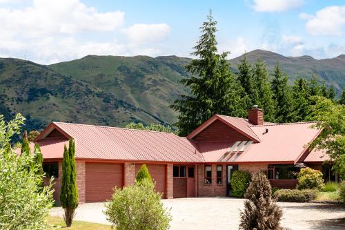 ein Haus mit rotem Dach und Bergen im Hintergrund in der Unterkunft Mountain Majesty on Orchard-Wanaka Holiday Home in Wanaka