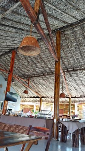 a restaurant with a straw roof with tables and chairs at Chalés Passagem do Canto in Barreirinhas