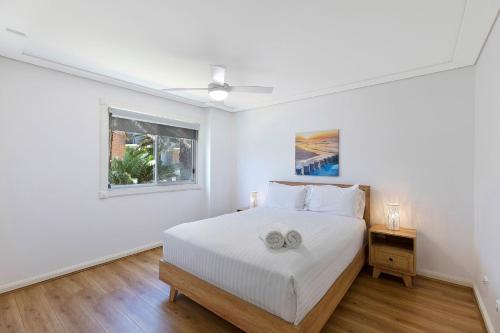 a white bedroom with a bed and a window at Sandy Cove Apartment The Entrance 8 in The Entrance