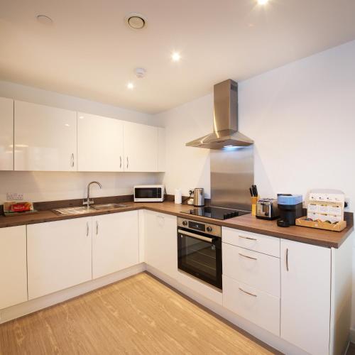 a kitchen with white cabinets and a stove top oven at Modern 1-Bed Apartment Near City Centre, Arndale, Spinningfields, MediaCityUK, Old Trafford & Etihad, Sleeps 4, Netflix, Gym, Balcony, Nespresso Machine, Perfect for Long & Short Stays, Leisure, Contractors & Professionals! in Manchester