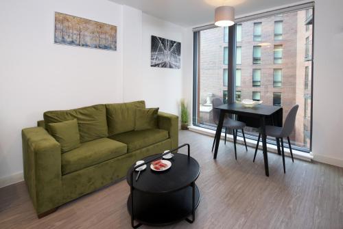 a living room with a green couch and a table at Modern 1-Bed Apartment Near City Centre, Arndale, Spinningfields, MediaCityUK, Old Trafford & Etihad, Sleeps 4, Netflix, Gym, Balcony, Nespresso Machine, Perfect for Long & Short Stays, Leisure, Contractors & Professionals! in Manchester