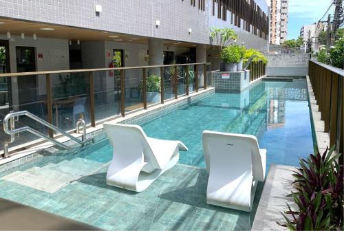 - une piscine dans un bâtiment avec 2 chaises blanches dans l'établissement Ponta Verde 250m praia I Feirinha do Artesanato I Piscina I Academia, à Maceió