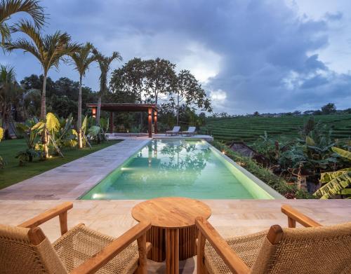 une piscine avec une table et des chaises à côté dans l'établissement Villa Famara Pererenan by Blacksand, à Tumbak Bayuh