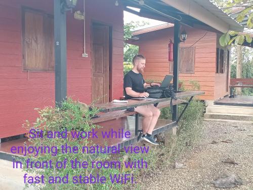 a man sitting at a picnic table with a laptop at Sleep & fishing Pua in Nan