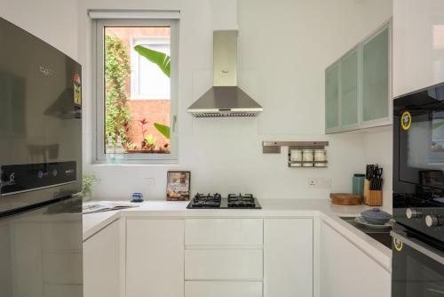 a white kitchen with white cabinets and a window at La Olalian 2 & 3 BHK Designer Villas Near Anjuna Beach with Private Pool & Sun Deck & Garden in Anjuna