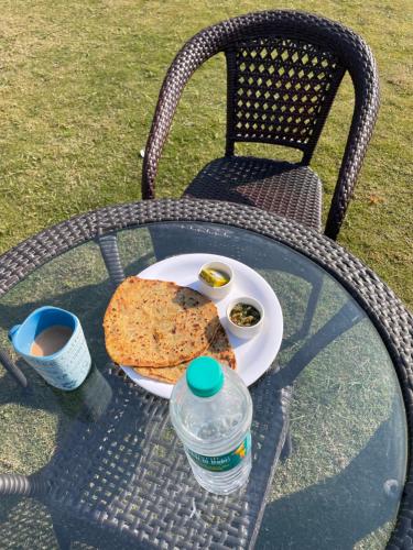 een tafel met een bord pizza en een fles water bij Aranyaa Cottage in Jait