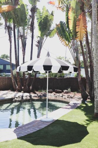 an umbrella in the middle of a pool with palm trees at Chalet Motel Brunswick Heads in Brunswick Heads