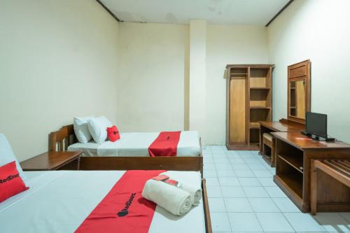 a room with two beds and a desk and a television at RedDoorz Plus at Mahajaya Hotel Denpasar in Denpasar