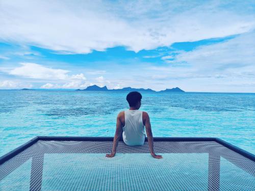 a person sitting on the edge of a boat in the ocean at Bubblefish Water Villa in Kampong Bum Bum